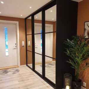 helsvart skyvedørsgarderobe i gang med speil på skyvedørene og tre horisontale felt avdelt med svarte sprosser